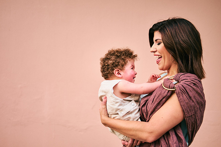 Una madre sonriente sosteniendo a su hijo pequeño delante de una pared rosa