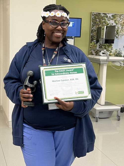 awardee wearing a headband of daisies, daisy award statue, and certificate.