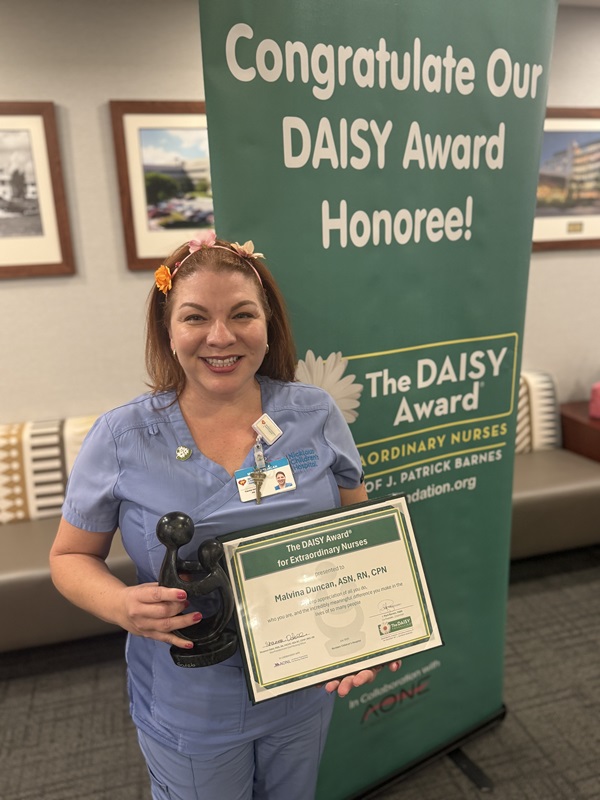 awardee wearing a headband of daisies, daisy award statue, and certificate.