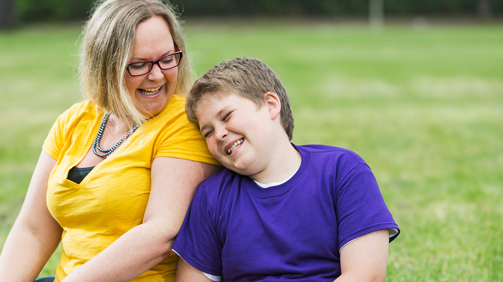 Niño con sobrepeso riendo e inclinándose hacia su mamá.