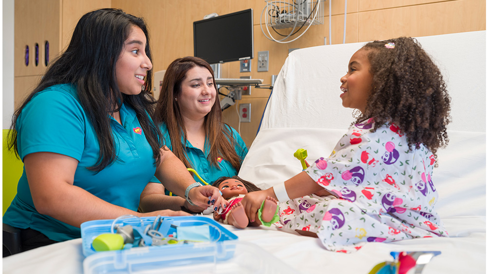 2 especialistas de vida infantil juegan con niña hospitalizada.