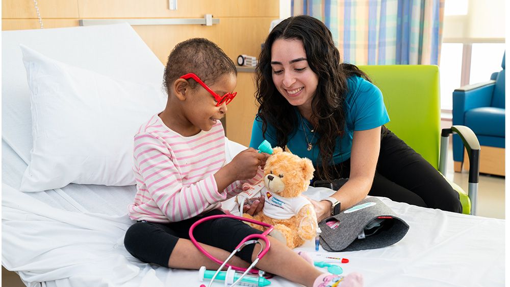 Especialista en Vida Infantil enseñando y jugando con niña en su cuarto de hospital.