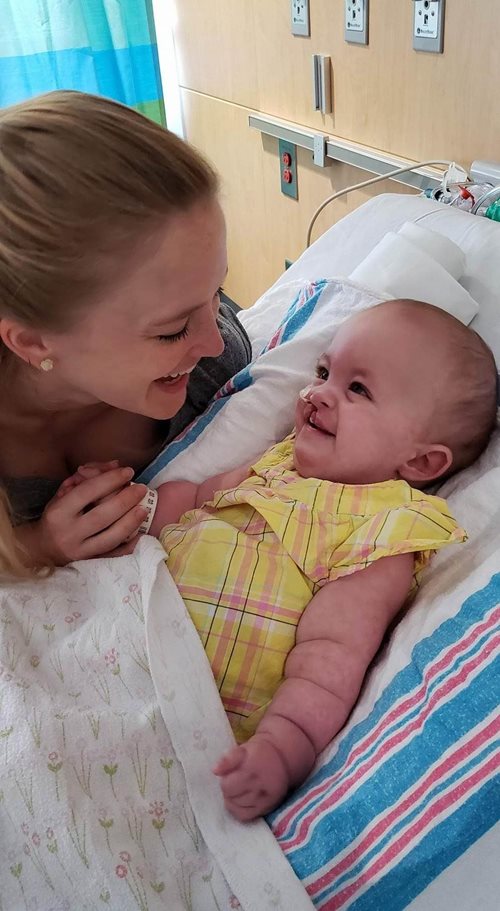 Heidi sonriendo y sosteniendo la mano de su madre en la cama del hospital